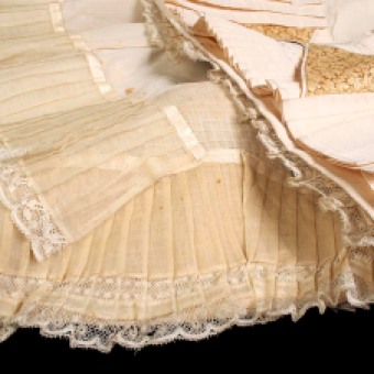 Around 1880, skirts were relatively slim down the legs but finished in a wide, sweeping train. To keep the train from folding in on itself and from wearing out on the floor, the floorside of the skirt was finished with rows and rows of ruffles. The term in French for the bottom ruffle is balayeuse, which means sweeper. This cotton ruffle was easily replaced once it wore out.